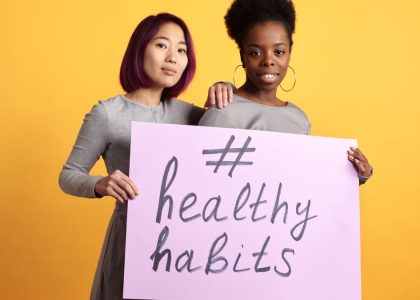 Two women holding a sign with '#healthy habits' on a vibrant yellow background.