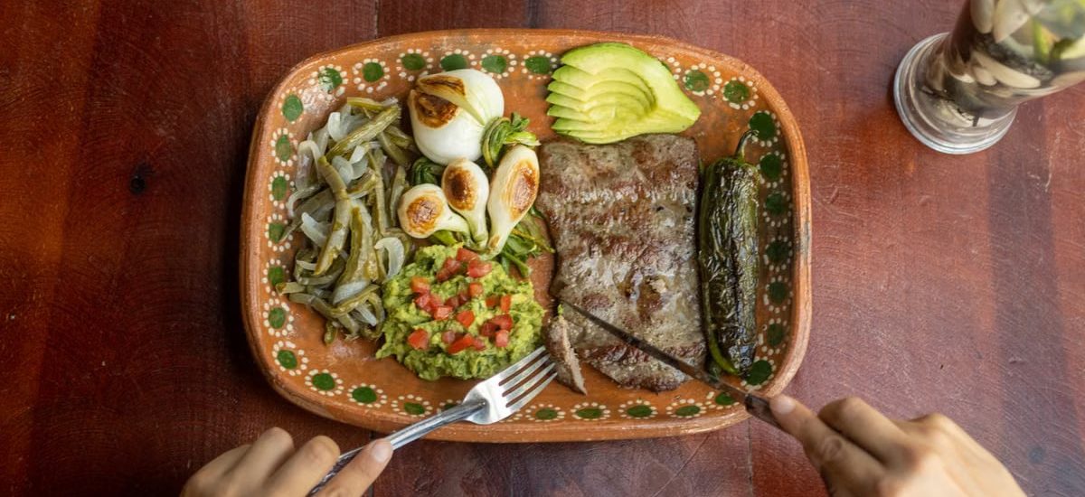 Authentic Mexican meal featuring grilled steak, avocado, and vegetables on a ceramic plate.