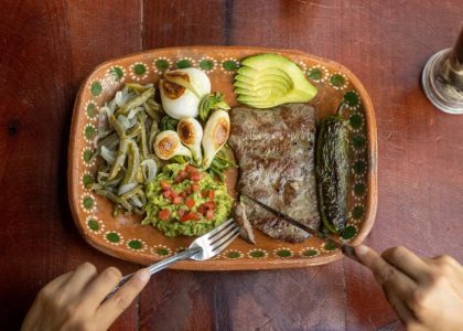 Authentic Mexican meal featuring grilled steak, avocado, and vegetables on a ceramic plate.